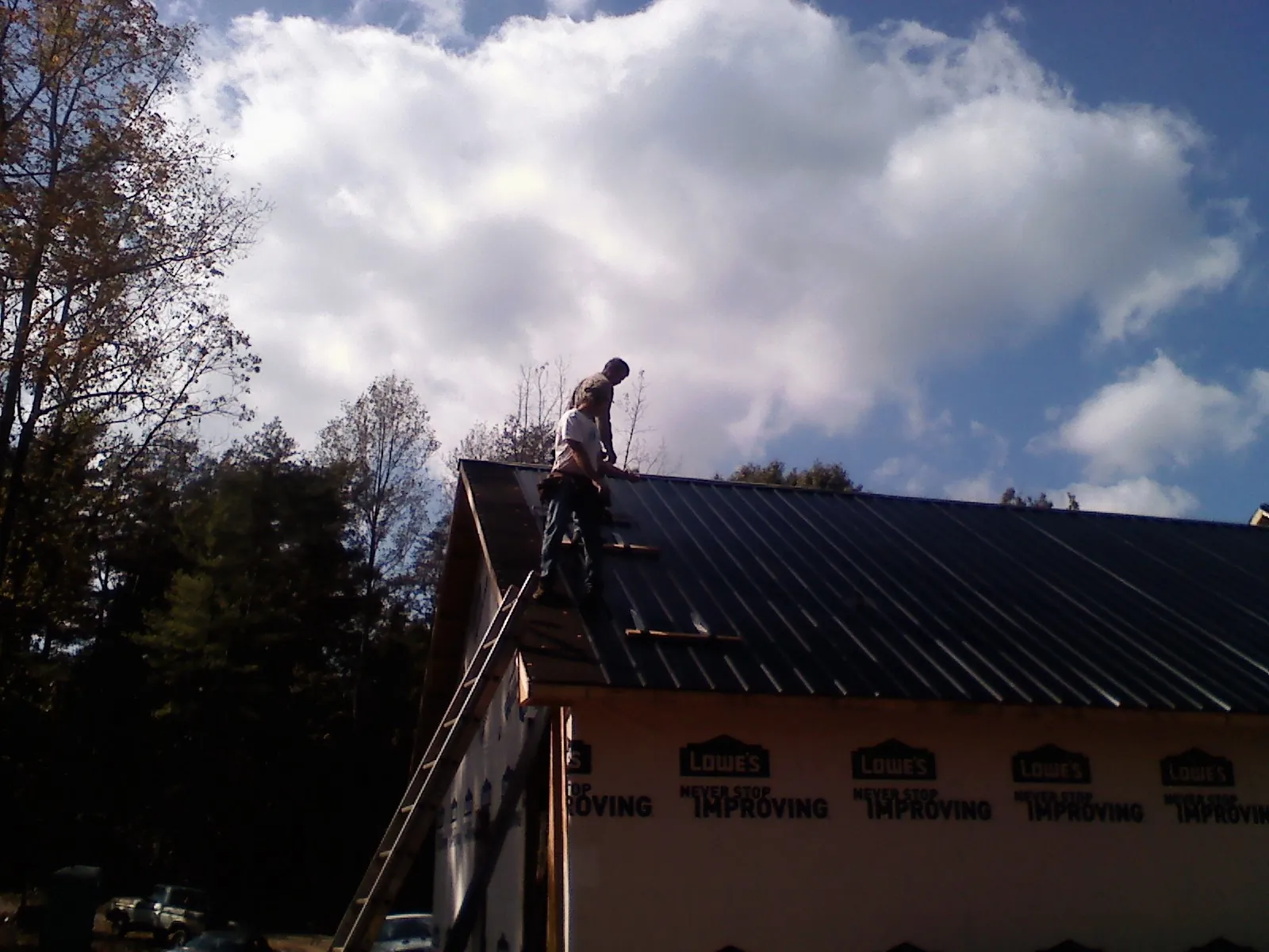 Roofer fastening dark metal panels high against a cloudy sky, from a Roof Inspection job in Reading